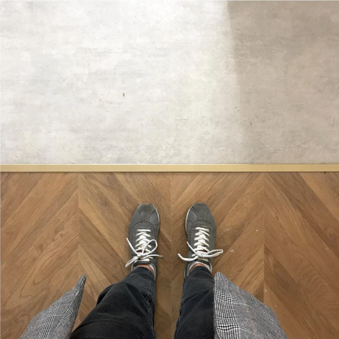 Imagen vista desde un punto de vista de ojo humano mostrando dos suelos, uno de ellos parquet, unos pantalones y unos zapatos